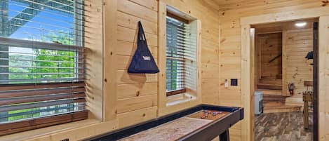 A wooden interior with a pool table, windows with blinds, and a hallway leading to another room.
