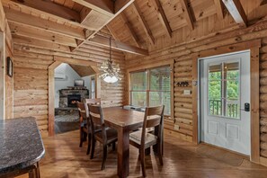 A wooden interior with a dining area featuring a table and chairs, a fireplace, and a view through a window. - Cozy Vilas Cabin with Hot Tub & Mountain Views (Vilas)