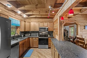 Une cuisine dotée de meubles en bois, de plans de travail en granit, d’appareils électroménagers en acier inoxydable et d’un luminaire suspendu rouge.