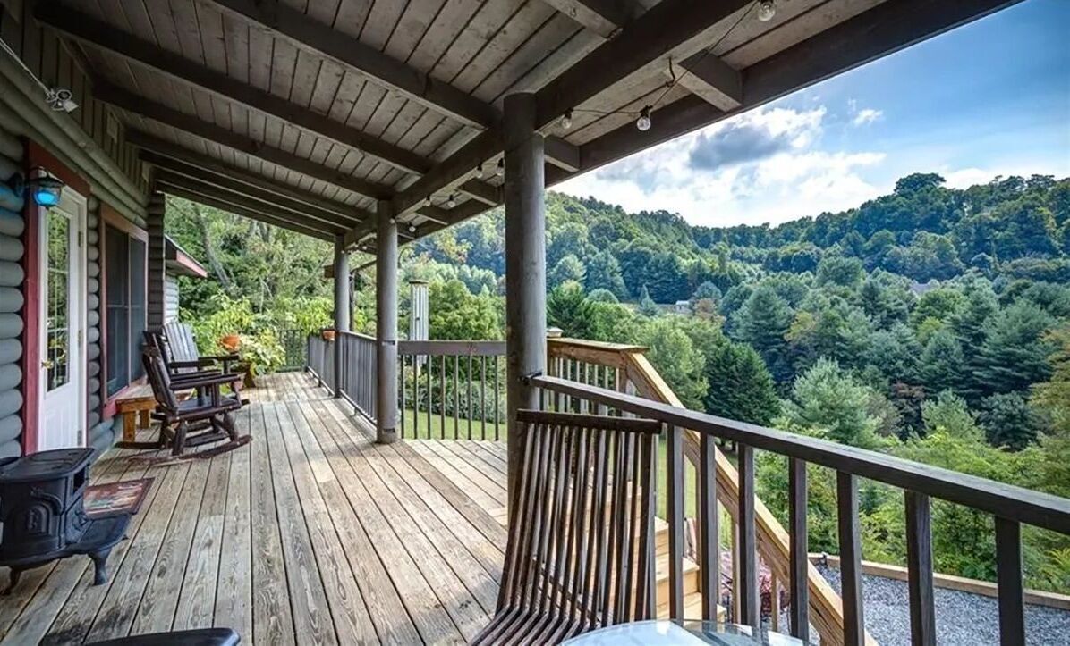 Covered wooden deck with rocking chairs overlooking tree-covered hills.