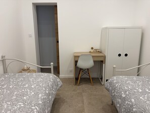 A bedroom with two beds, a desk, a chair, and a wardrobe.