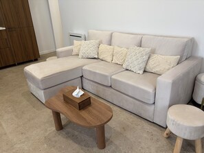 Ein modulares Sofa mit Couchtisch aus Holz und einem kleinen Hocker in einem farblich neutral gestalteten Raum.