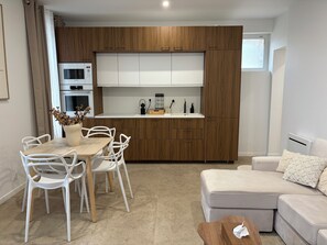 A modern kitchen with wooden cabinets, a dining area with white chairs, and a white sofa.