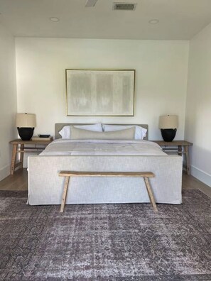 Slaapkamer met een groot bed, twee nachtkastjes, een hoofdbord, een vloerkleed en een kunstwerk aan de muur.