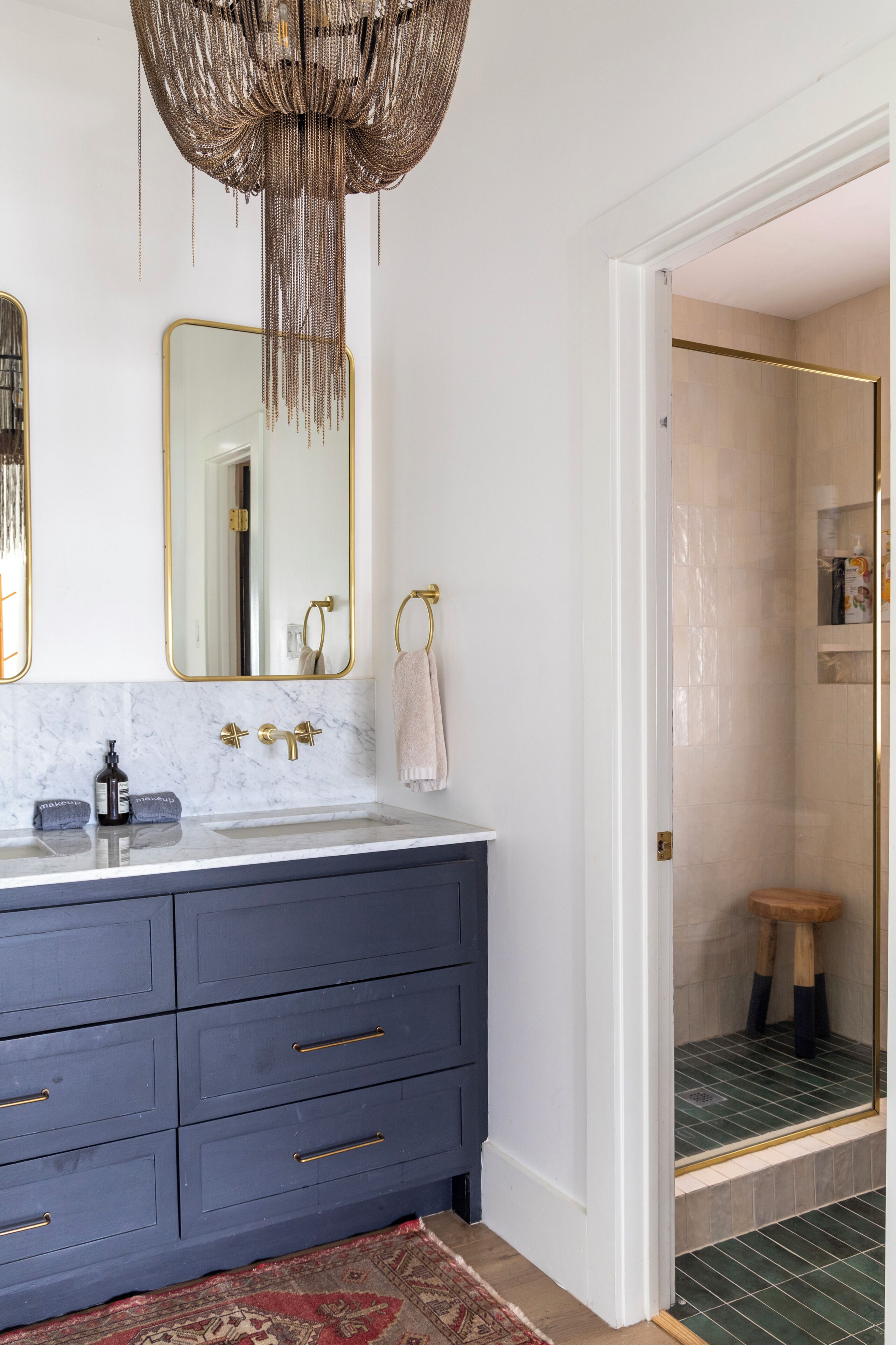 Une salle de bain dotée d’un comptoir en marbre, de robinetterie dorée et d’un lustre suspendu.