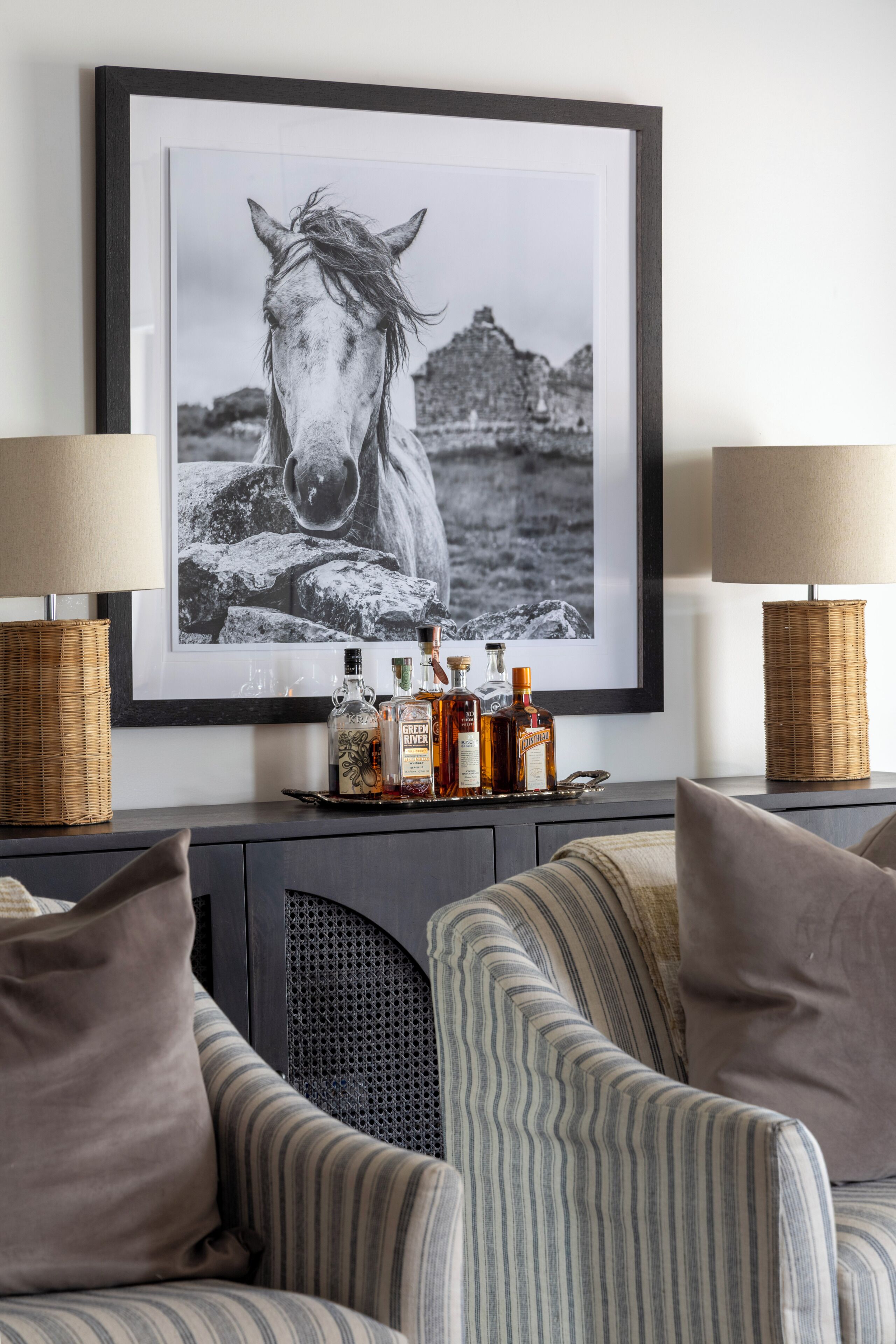 A framed black and white horse portrait on a wall, flanked by two lamps and a tray of liquor bottles.