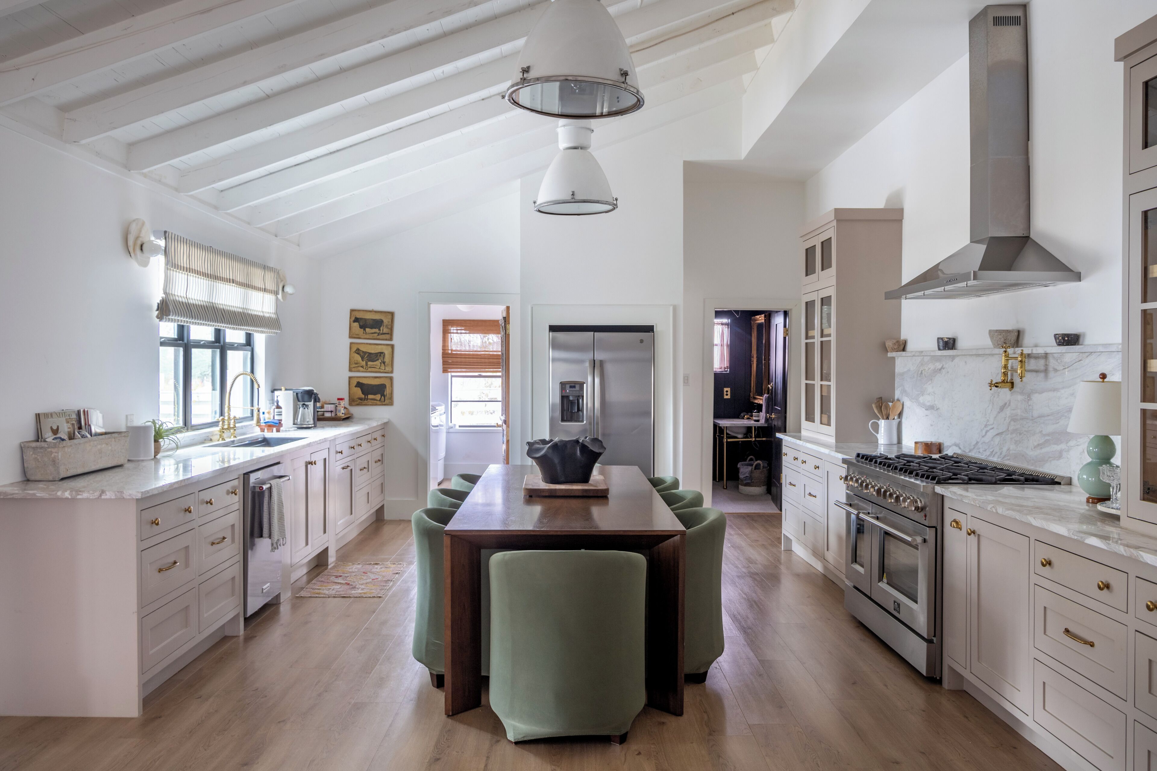 A spacious kitchen with high ceilings, a dining area with green upholstered chairs, and a modern stove.