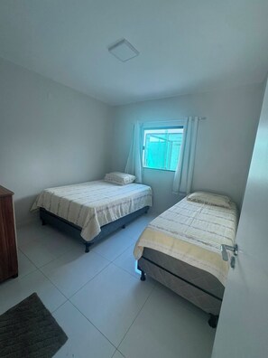 A room with two beds, a window with curtains, and a radiator. - House in a gated community in Lençóis Maranhenses with a swimming pool and 4 suites. (Barreirinhas)