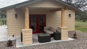 A covered outdoor seating area with a sofa, two side tables, and a small fire pit.