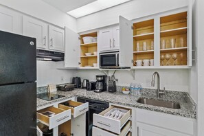 Une cuisine moderne avec des meubles blancs, un réfrigérateur noir, des plans de travail en granit et des appareils électroménagers intégrés, notamment un four à micro-ondes et une machine à café.