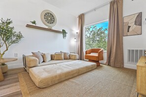 Ein modernes Schlafzimmer mit einem Bett, einer Couch, einem Sessel, einer Pflanze und einer Wanduhr.