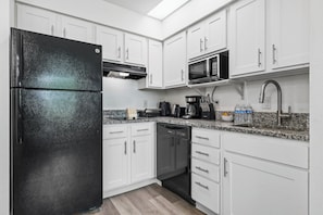Eine moderne Küche mit weißen Schränken, einem schwarzen Kühlschrank, einer Mikrowelle und einer Kaffeemaschine.