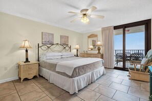 A bedroom with a bed, two bedside tables with lamps, a ceiling fan, a balcony with outdoor furniture, and a large window. - Phoenix VII Condo 605 (Orange Beach)