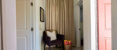 A hallway with a door, a chair with cushions, a basket with striped items, and a curtain.