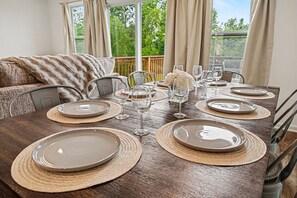 A dining table set with plates, glasses, and a centerpiece, with a view of greenery outside.