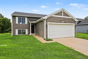 A two-story house with a garage, a front door, and a small front yard.