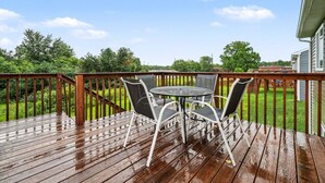 Terraza de madera con mesa y sillas, rodeada por barandilla de madera, con vista a un jardín.