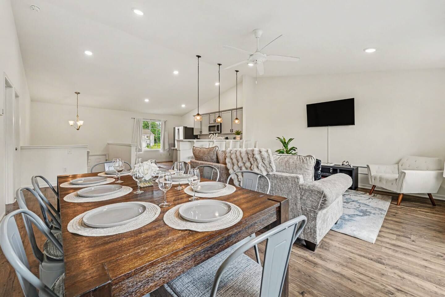 A modern dining area with a wooden table set for six, surrounded by grey upholstered chairs.