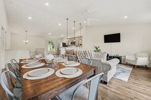 A modern dining area with a wooden table set for six, surrounded by grey upholstered chairs.