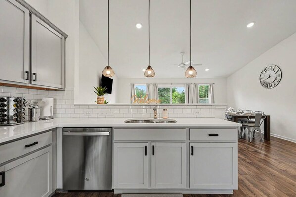 A modern kitchen with white cabinetry, a stainless steel dishwasher, and pendant lighting.