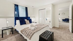 Un dormitorio moderno con una cama grande, una mesita de noche, un espejo, una silla y una puerta que da a otra habitación.