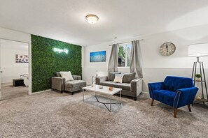 A modern living room with a green wall, grey sofas, a blue armchair, a coffee table, and a floor lamp.
