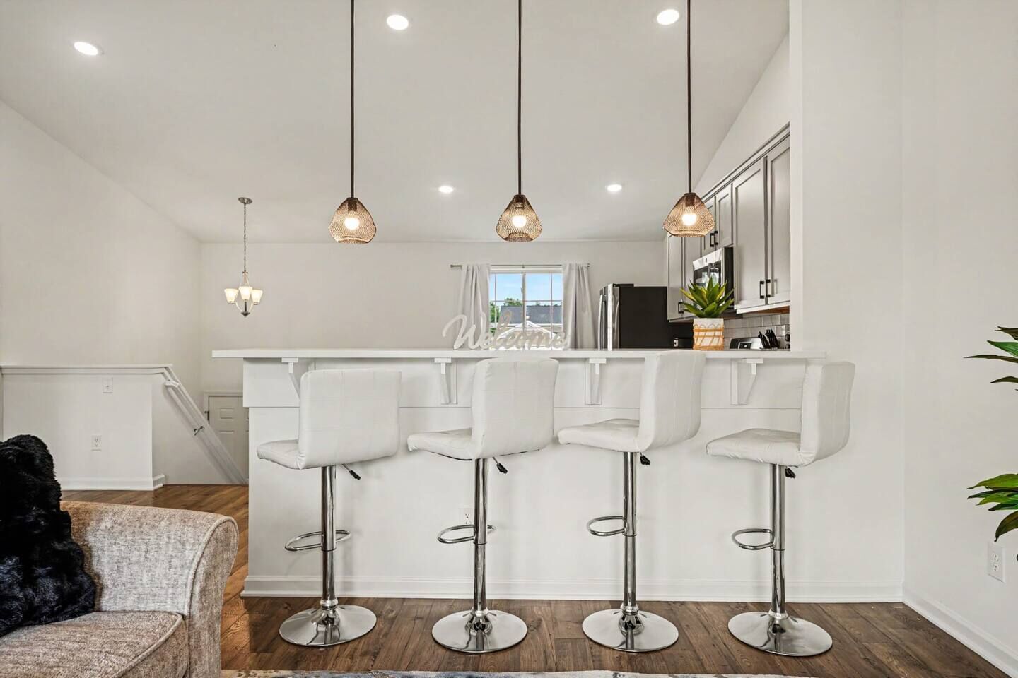 A modern kitchen with white bar stools, pendant lighting, and a view to the outside.