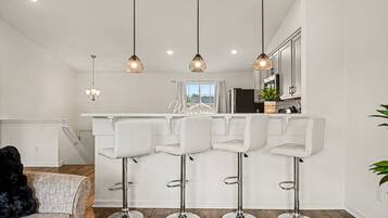 A modern kitchen with white bar stools, pendant lighting, and a view to the outside.
