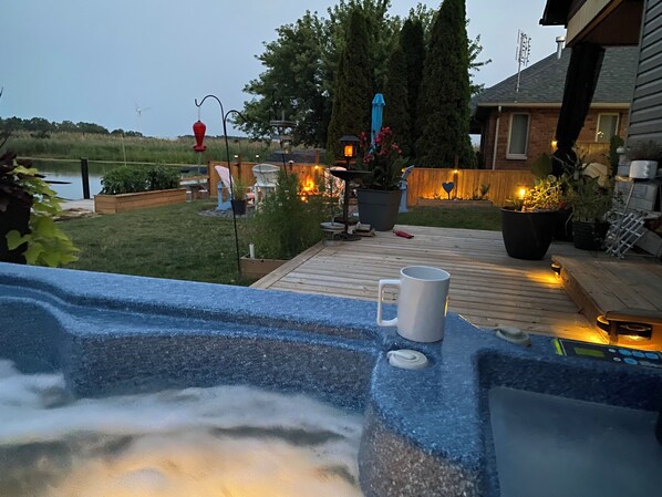 A hot tub with a white mug on the edge, surrounded by a wooden deck with potted plants and outdoor lighting.