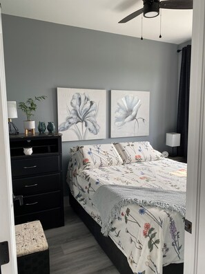 A bedroom with a bed, dresser, nightstand, and two wall-mounted flower paintings.
