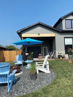 A backyard with a patio area, outdoor furniture, and a house with a garage.