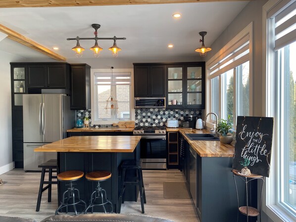 A modern kitchen with a central island, bar stools, and a chalkboard sign.