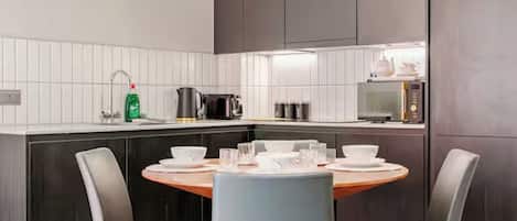 Una cocina moderna con salpicadero de azulejos blancos, armarios oscuros y una mesa redonda con sillas.