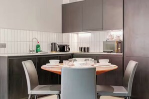 Cozinha moderna com painel de azulejos brancos, armários escuros e uma mesa de jantar redonda com cadeiras.