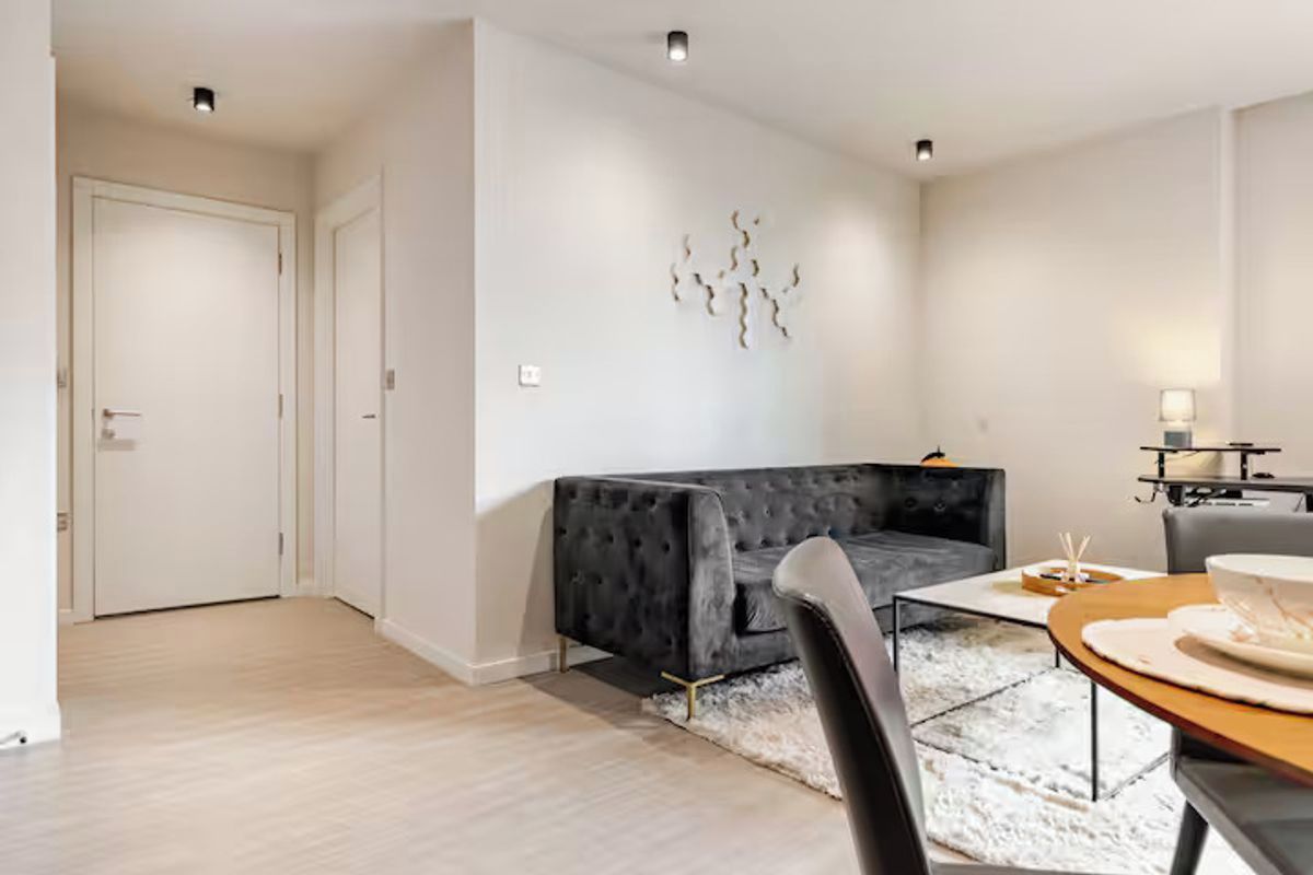 Una sala de estar moderna con un sofá gris oscuro, una mesa redonda de madera y una alfombra blanca.