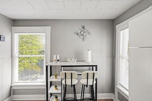 A kitchen with a white marble countertop, two bar stools, a decorative wall piece, and a window with blinds.