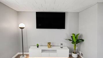 A modern living room with a white entertainment unit, a flat-screen TV mounted on the wall, a floor lamp, and a potted plant.