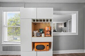 A kitchen with a built-in microwave, a coffee maker, and a shelf with kitchen items.