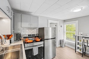 A modern kitchen with grey cabinets, a stainless steel refrigerator, and a window with blinds.
