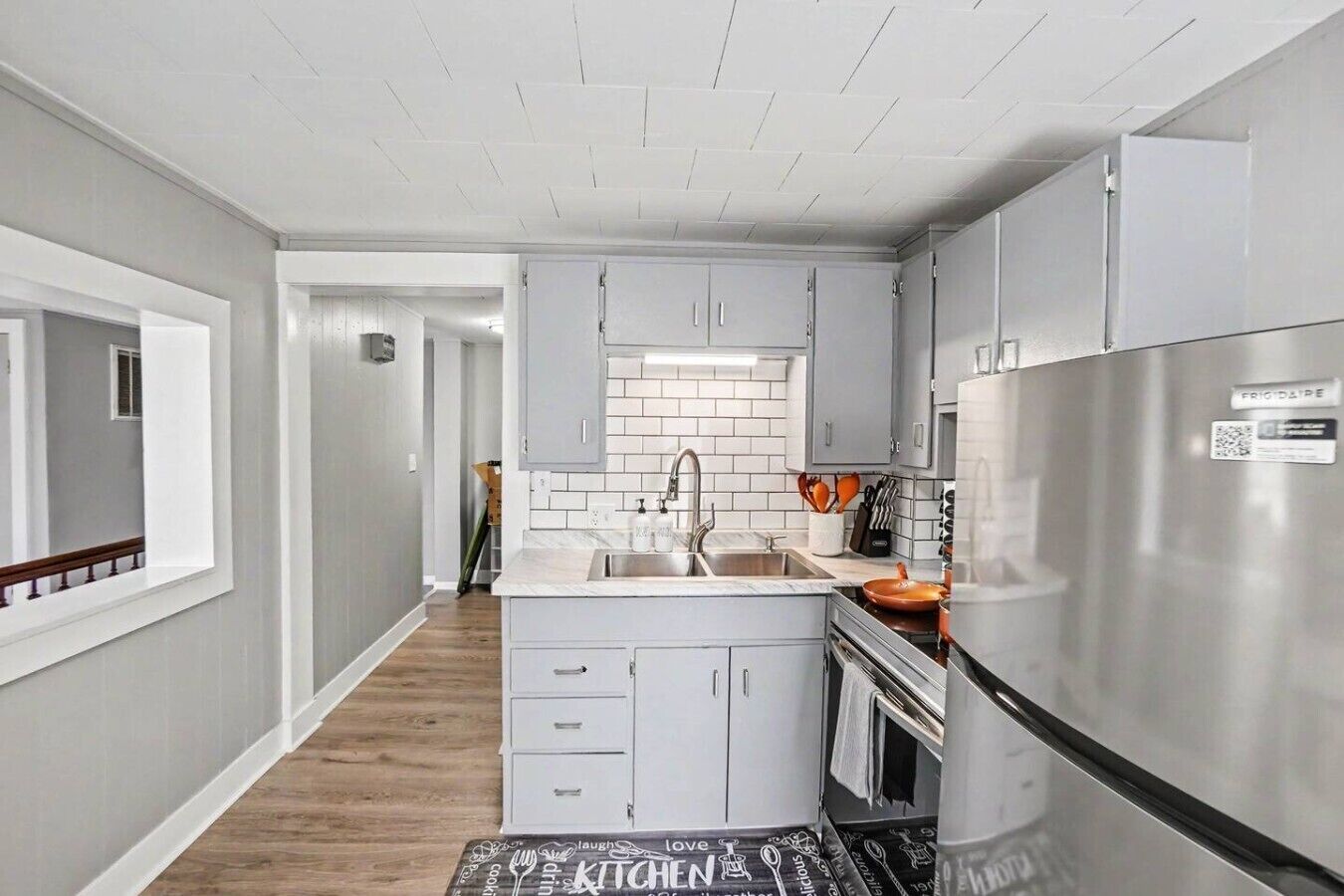 A modern kitchen with grey cabinets, a stainless steel refrigerator, and a tiled backsplash.