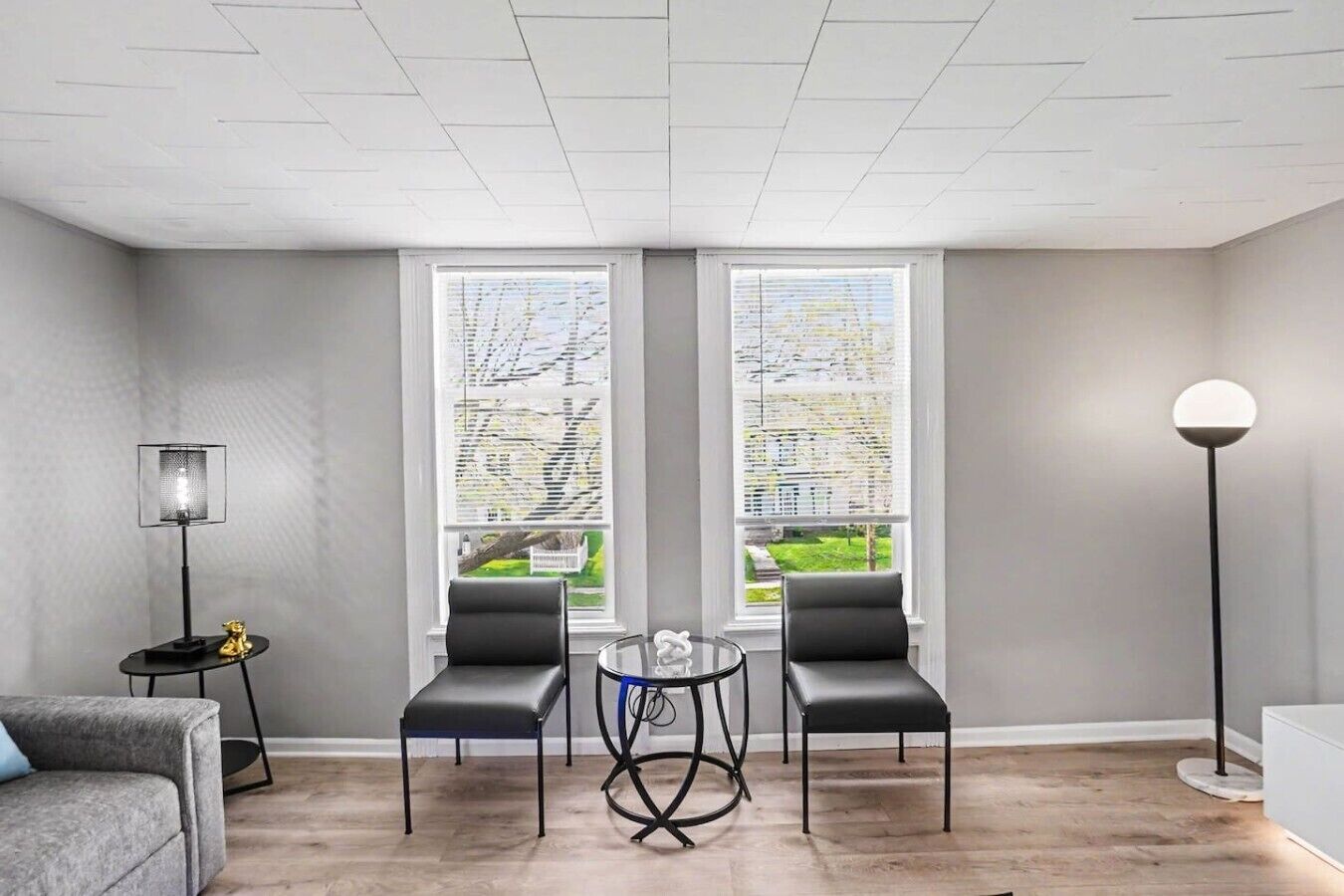 Un salon moderne avec deux fauteuils noirs, une petite table ronde, un lampadaire et un canapé.