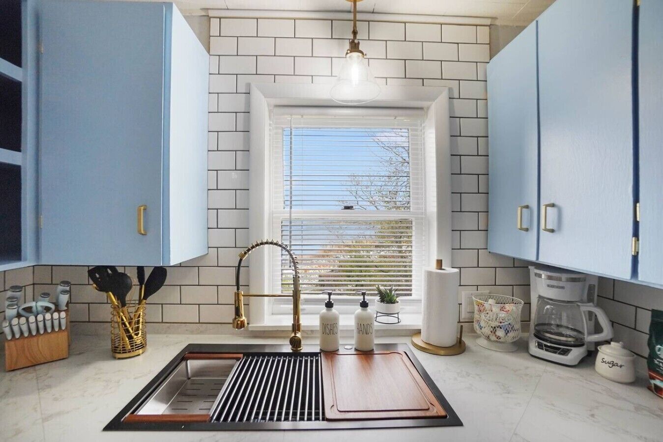 A kitchen with a window, a sink with a gold faucet, and cabinets.