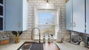 A kitchen with a window, a sink with a gold faucet, and cabinets.