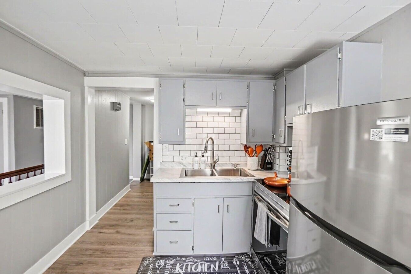 A modern kitchen with grey cabinets, a stainless steel refrigerator, and a tiled backsplash.