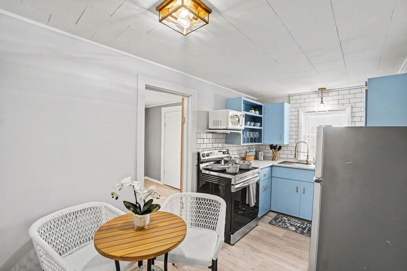 A compact kitchen with white cabinets, a stove, and a refrigerator. There is a dining area with a round table and chairs, and a small potted plant.