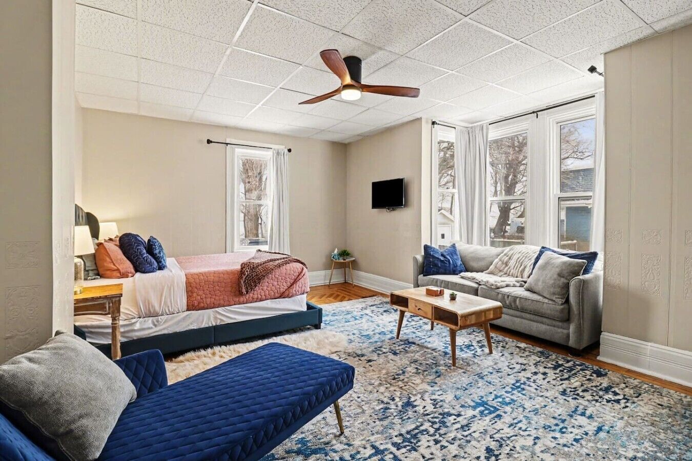 A room with a bed, two sofas, a coffee table, and a ceiling fan.