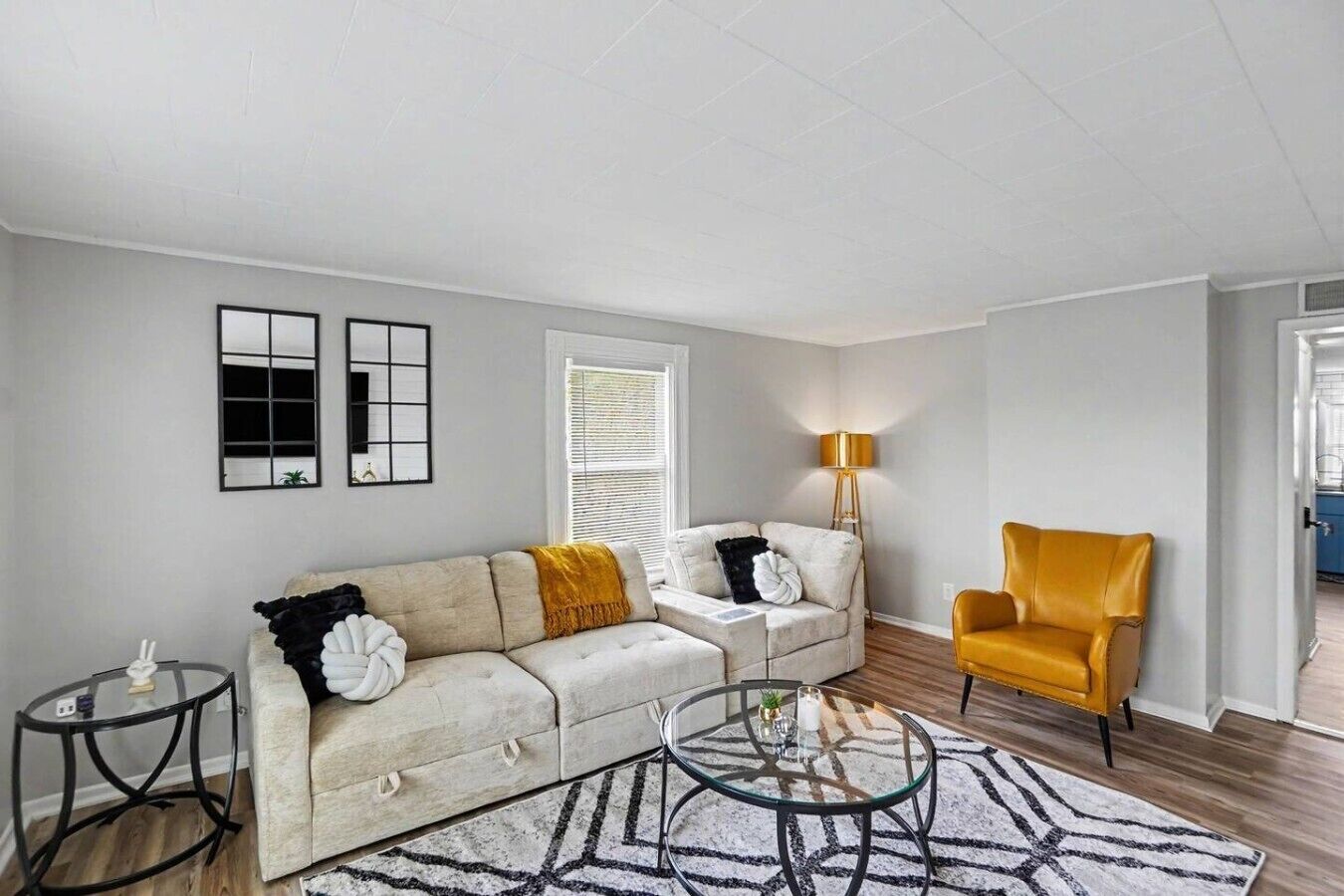 A living room with a sofa, a round coffee table, a yellow armchair, and a lamp.