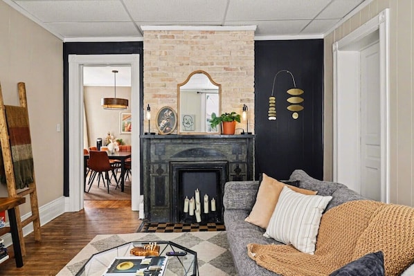 A living room with a fireplace, a sofa, a coffee table, and a dining area in the background.