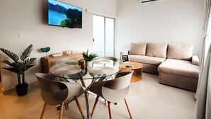 Een moderne woonkamer met een glazen eettafel, een bank en een televisie aan de muur.