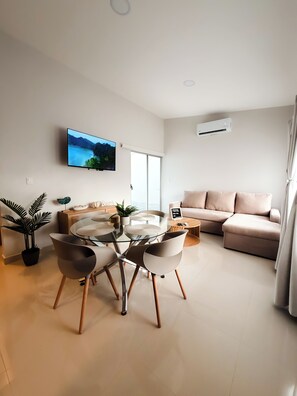 A modern living room with a glass dining table, a sofa, and a TV mounted on the wall. - Brand New: Boutique House, Near LIR Airport & Best Beaches (Guanacaste Province)